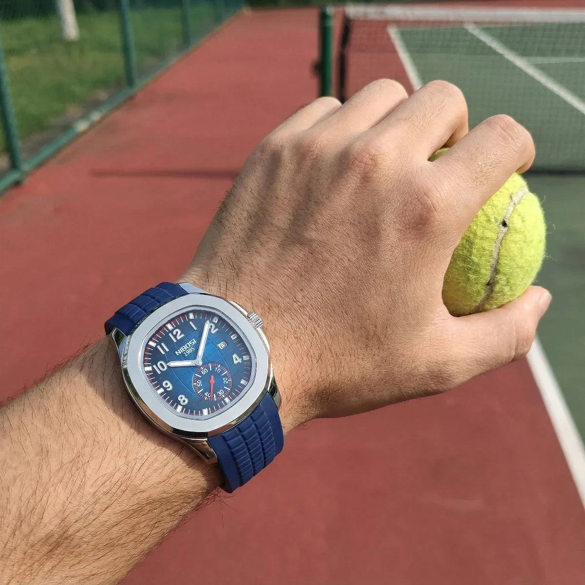 Blue-dial watch on the wrist holding a tennis ball