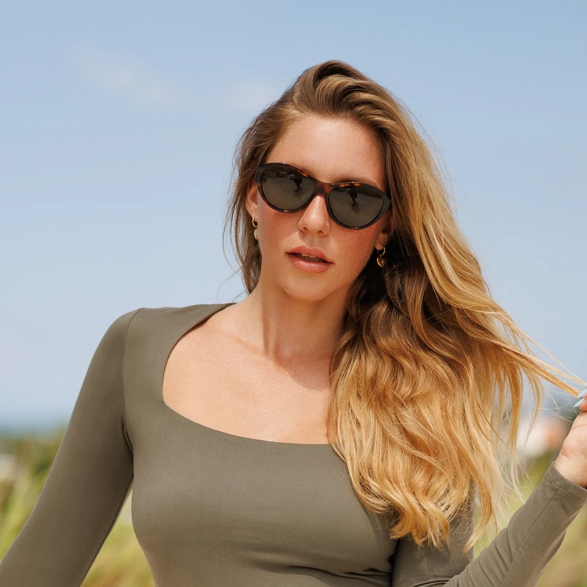 Woman in an olive top wearing cat eye sunglasses outdoors