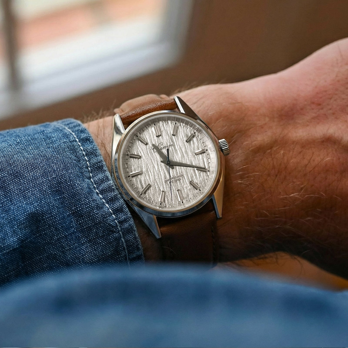 Silver bark-dial watch on the wrist with a denim cuff