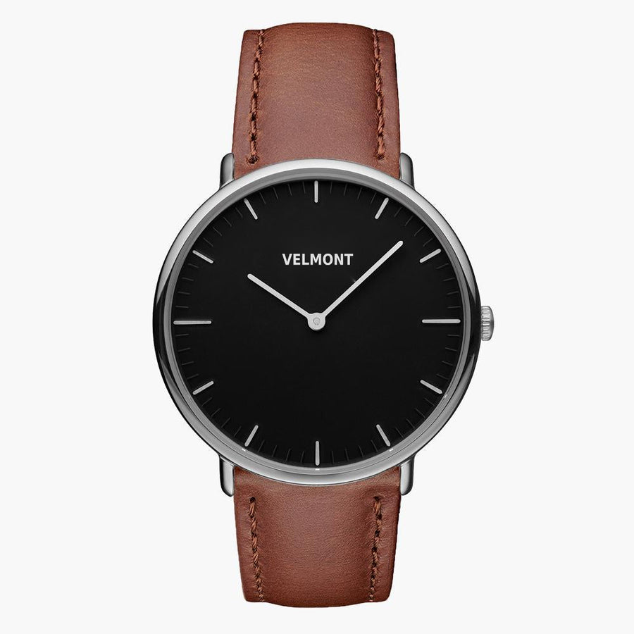A black dial framed by a slim silver-tone case, set on a brown strap.