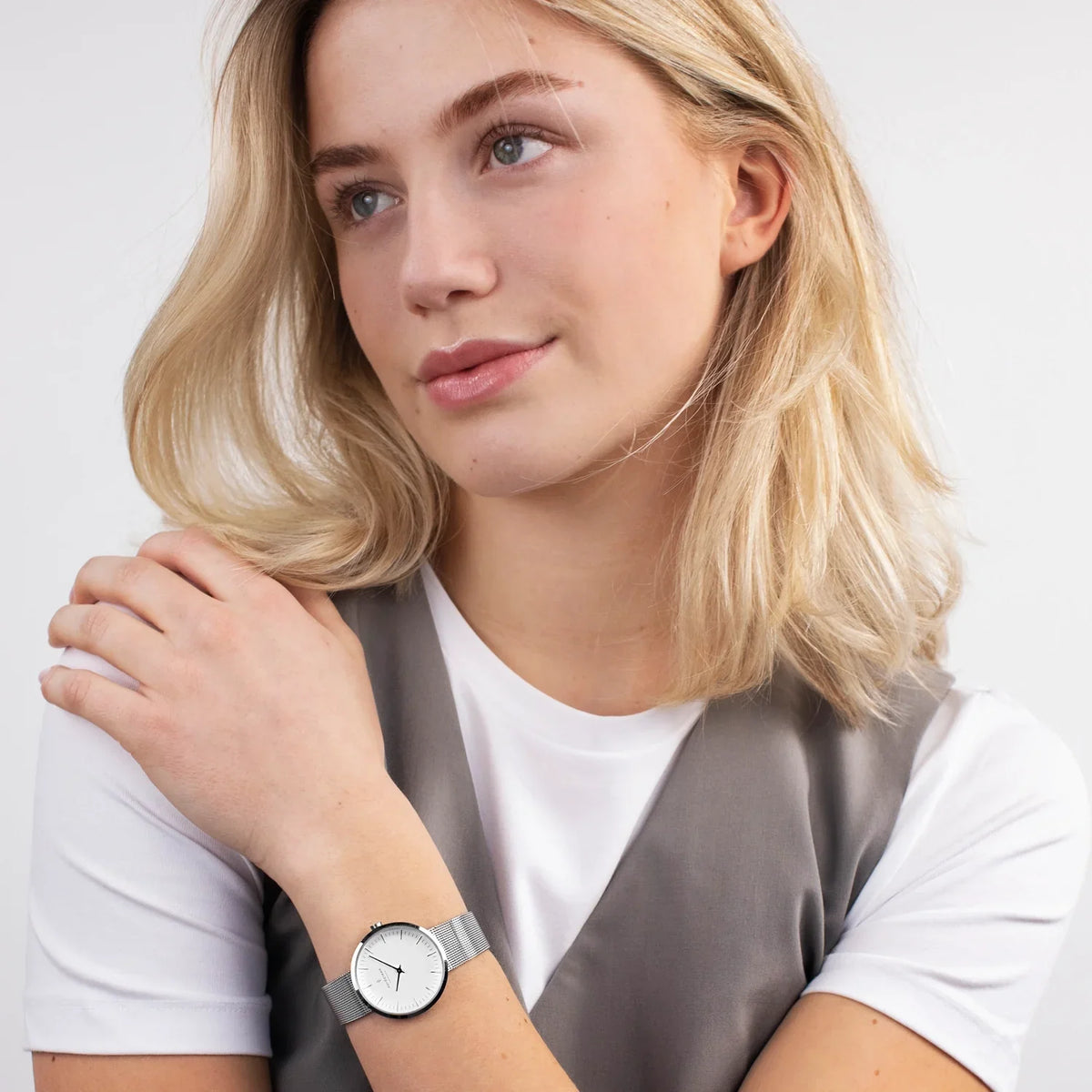 Woman in a white tee and gray vest wearing the silver-tone watch.