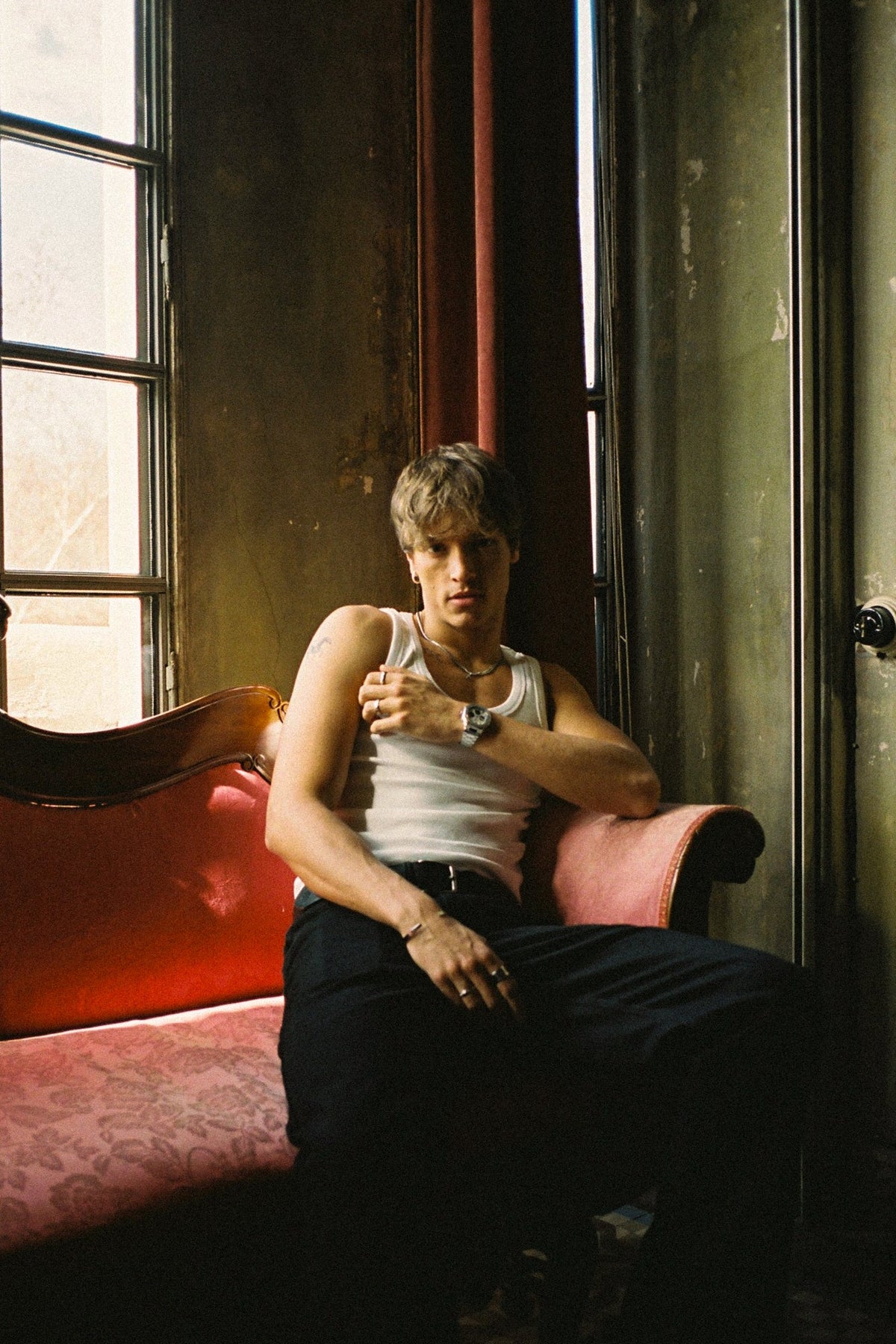Man seated on a red sofa by a window, watch visible