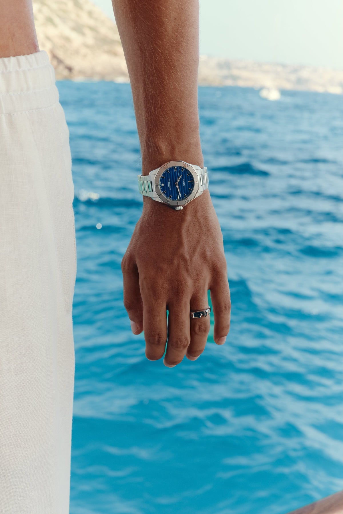 Hand by the water wearing the blue-dial watch