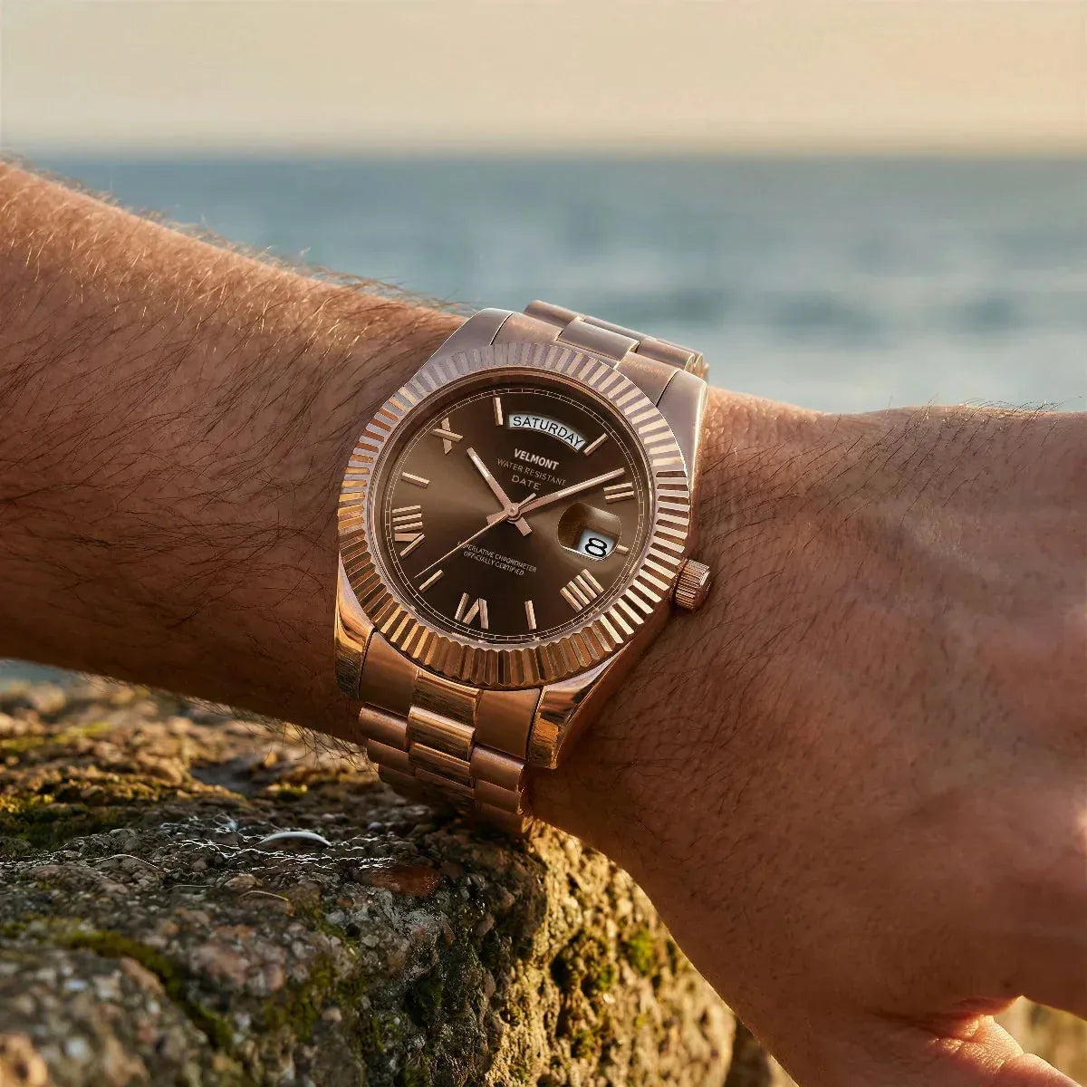 Rose gold-tone watch on a wrist by the sea