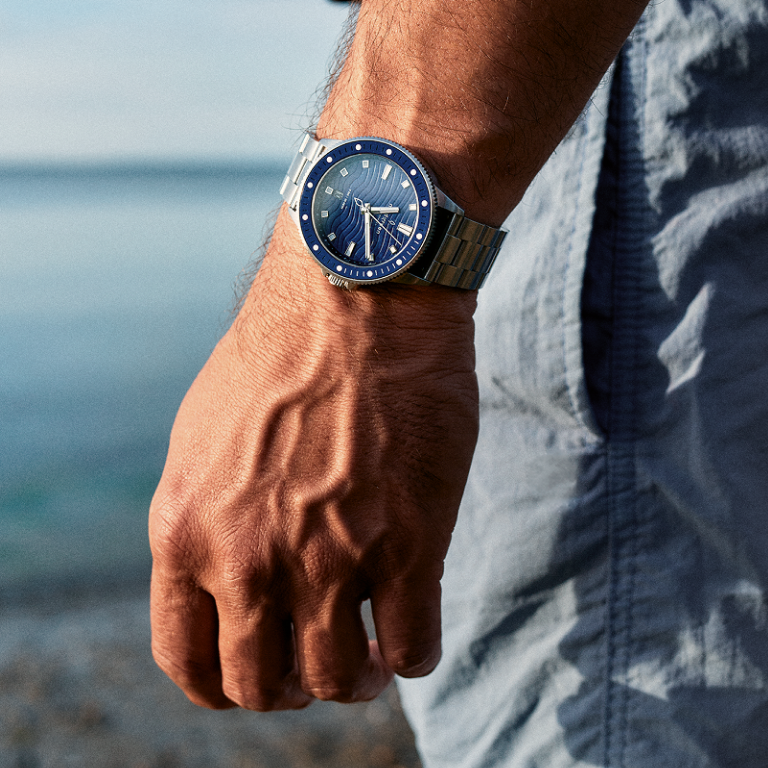 Worn by the sea on a relaxed wrist beside light denim shorts.
