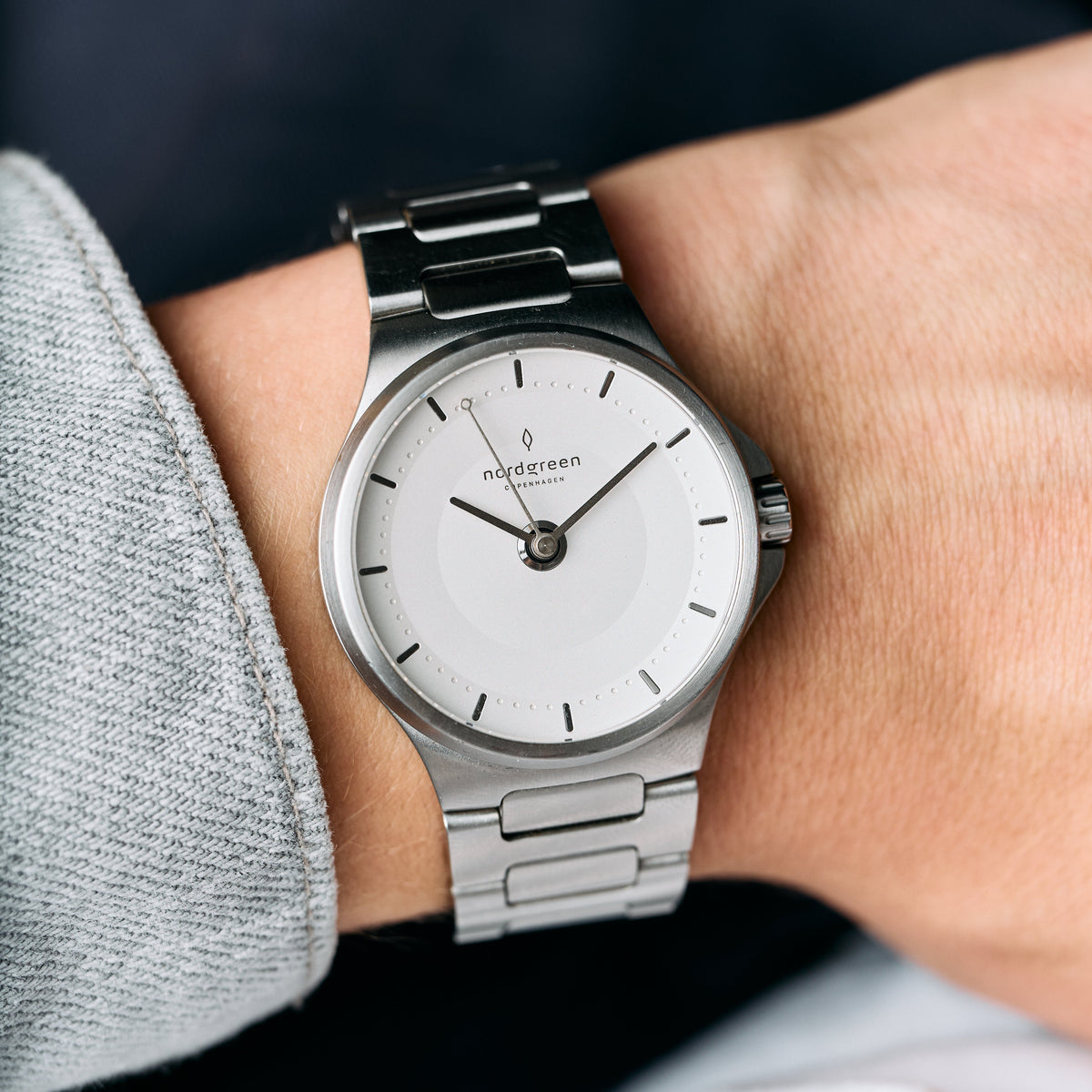 Close view of the watch on a wrist beside a gray sweater sleeve.