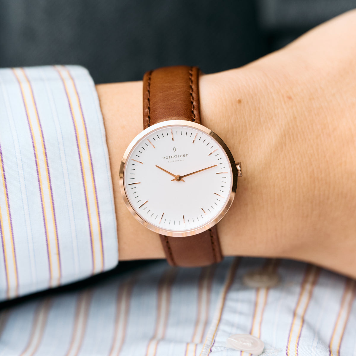 The watch worn on a wrist with a striped shirt cuff.