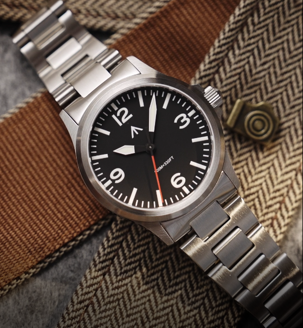 Pilot-style watch on a steel bracelet resting on herringbone fabric