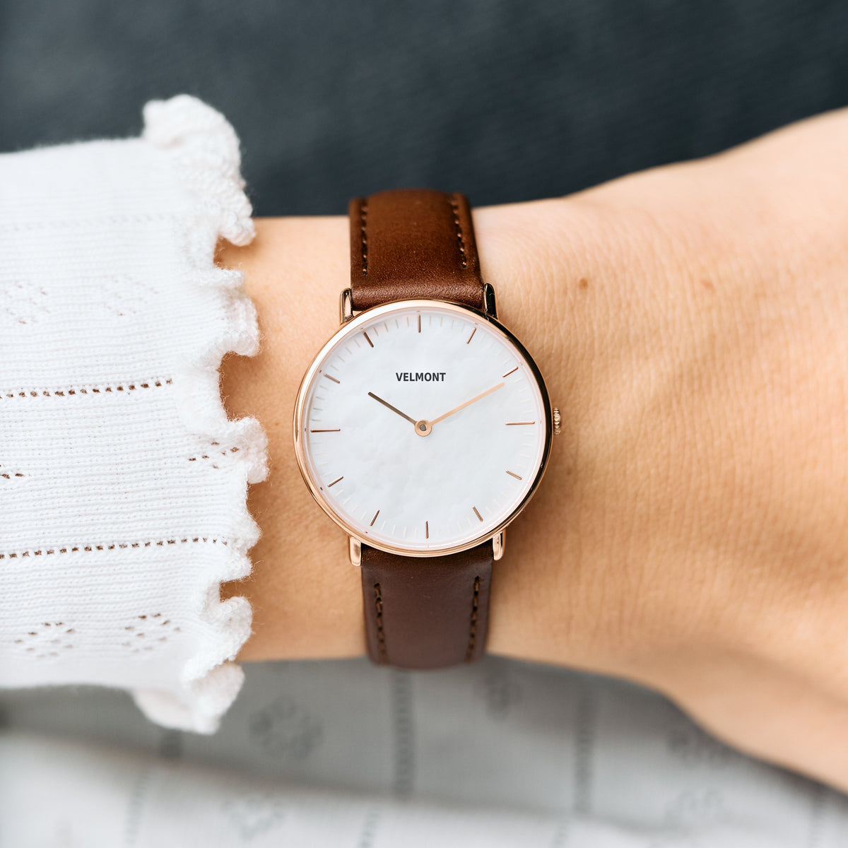 Worn on a wrist with a white ruffled cuff, brown strap and rose gold-tone case.
