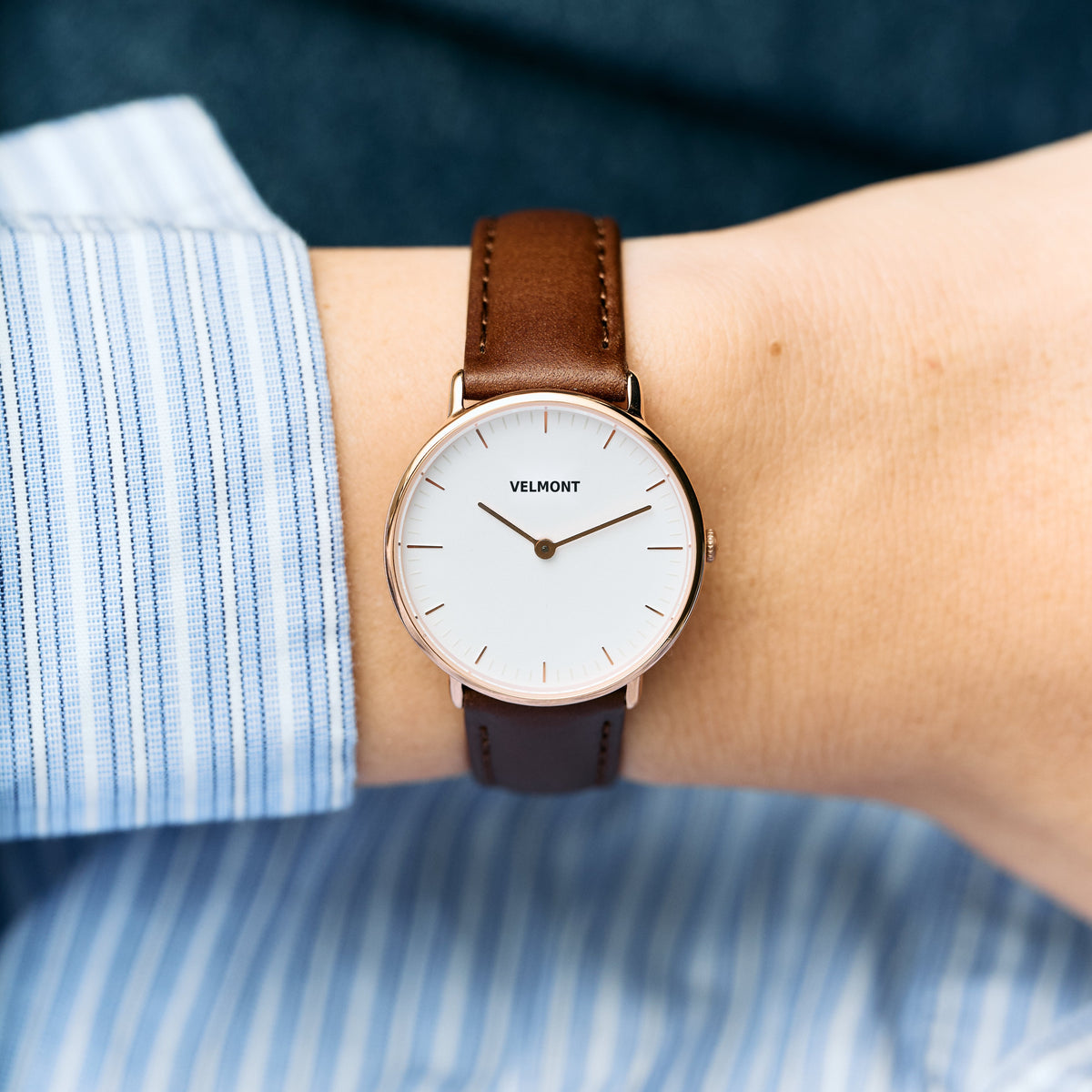 Small white-dial watch worn with a blue striped shirt and brown strap.