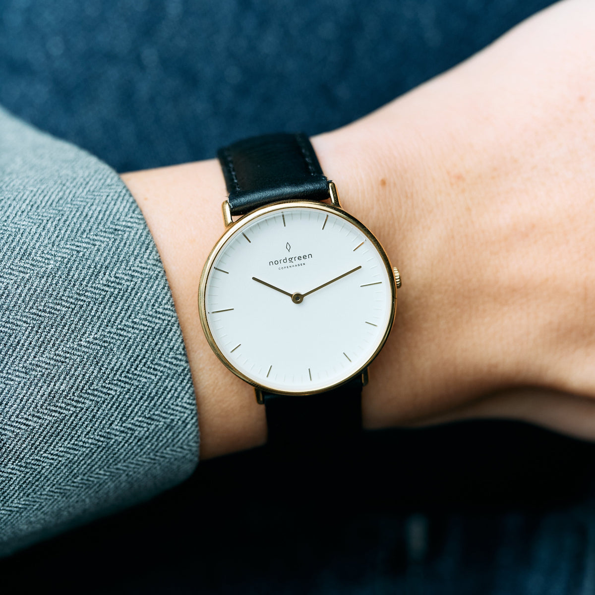 The watch worn on a wrist beside a gray herringbone jacket sleeve.