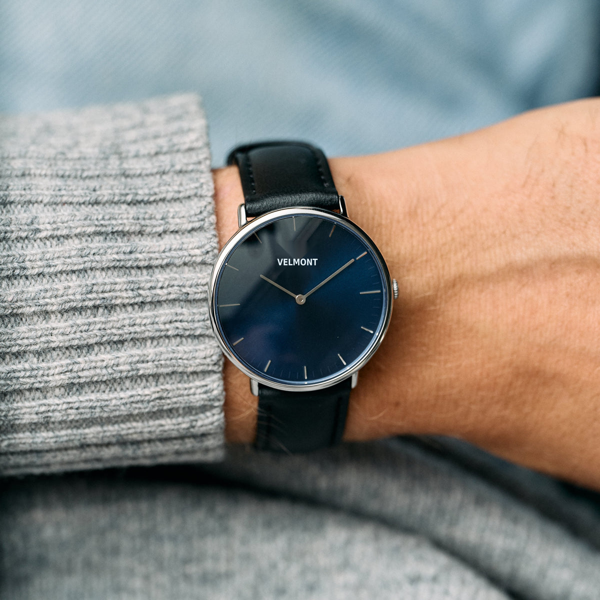 The blue-dial watch worn on a wrist beside a gray knit sweater cuff.