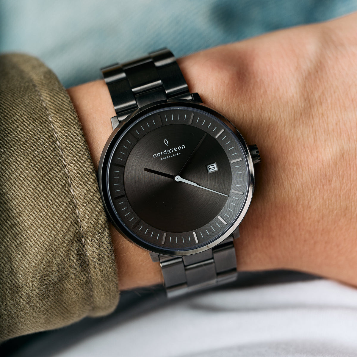 Gray-dial watch worn on a wrist next to an olive jacket cuff.