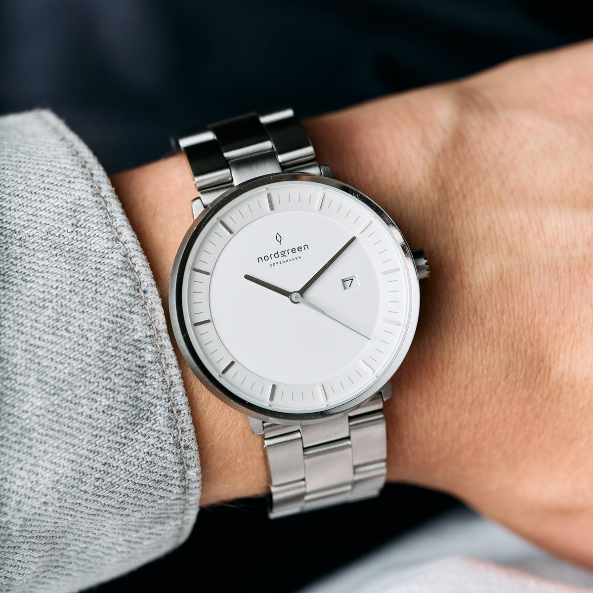 The white-dial watch on a wrist with a gray sweatshirt sleeve.