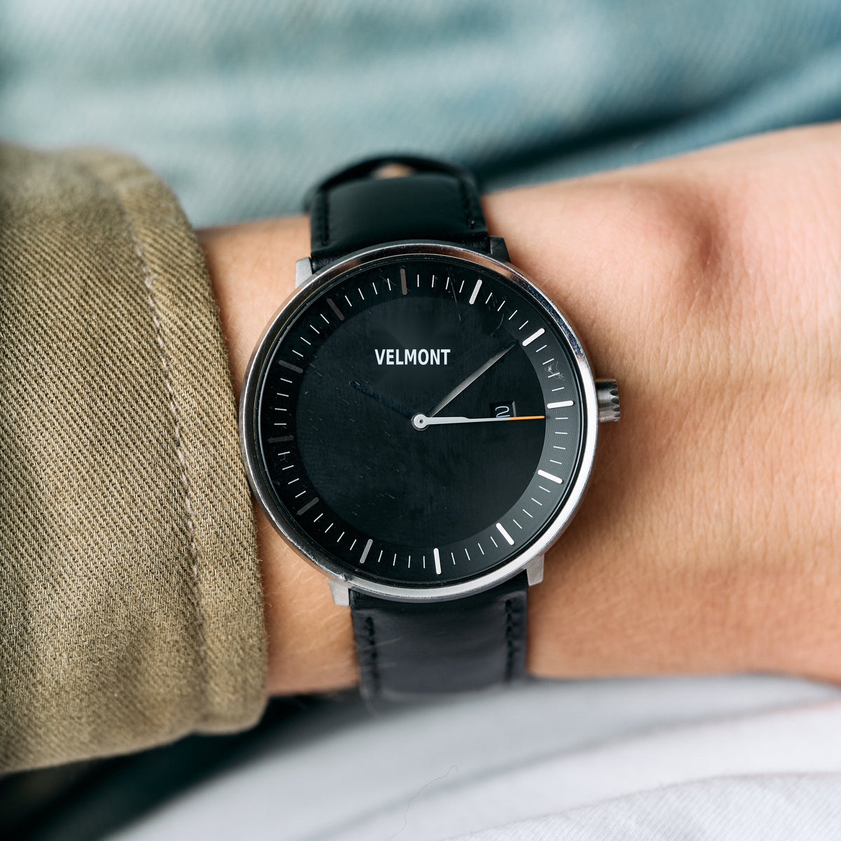 Worn on a wrist beside an olive jacket sleeve, black dial facing up.