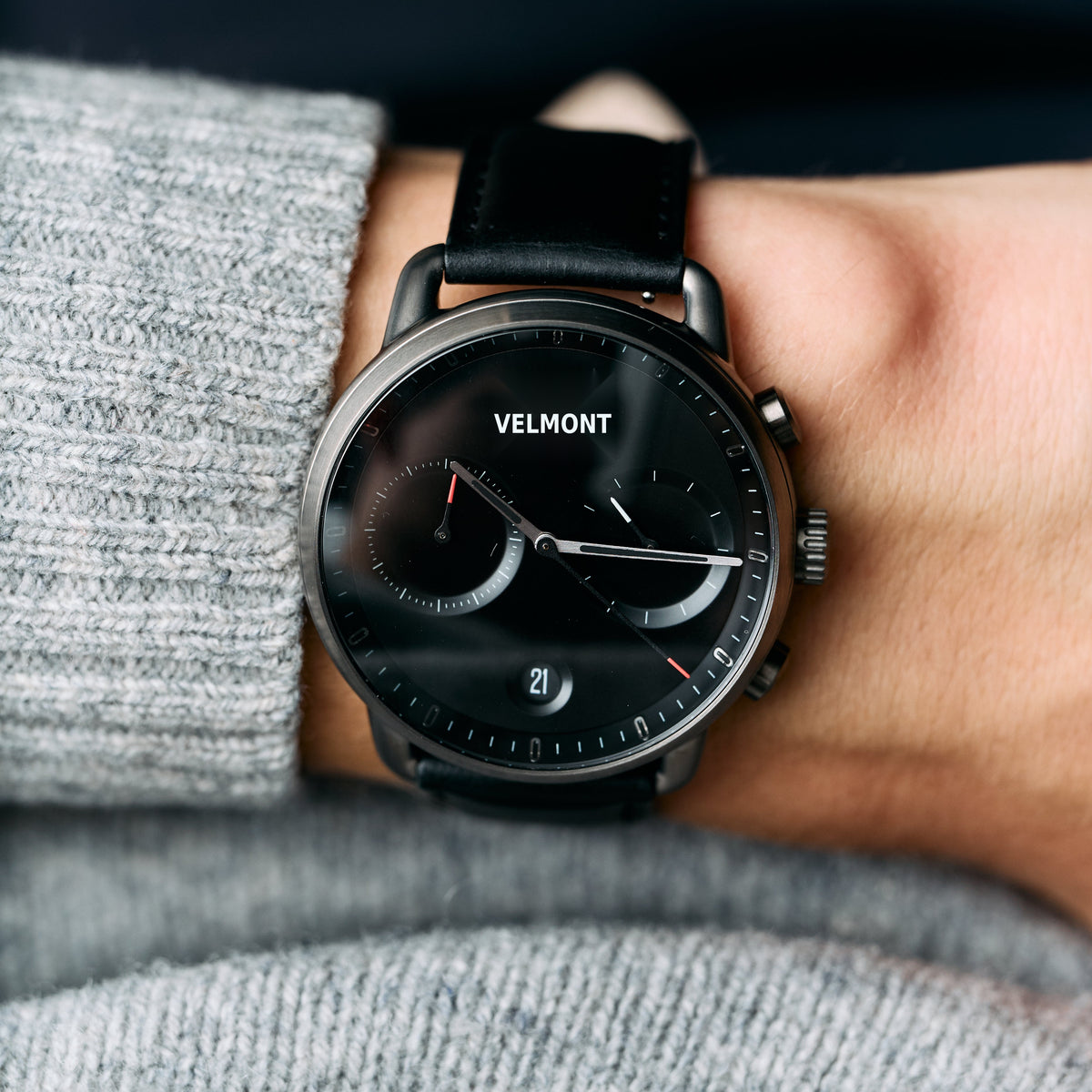 The all-dark watch worn on a wrist beside a gray knit sweater.