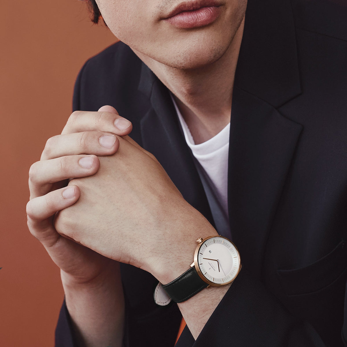 Man in a dark blazer with clasped hands, wearing the rose gold-tone watch.