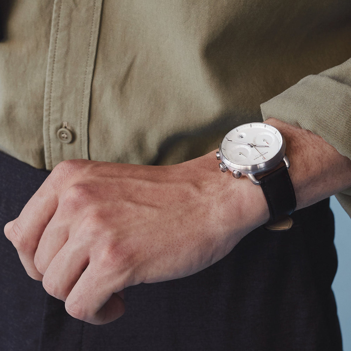 A man in an olive shirt wearing the white dial watch on a black strap.