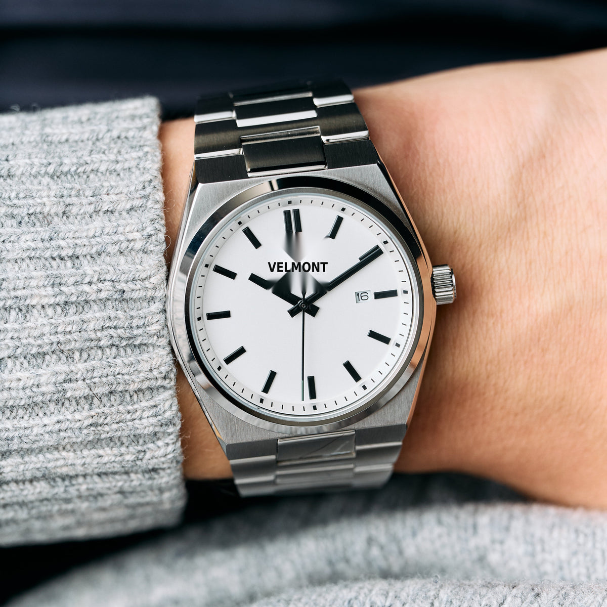 The watch on a wrist next to a gray knit sweater sleeve.
