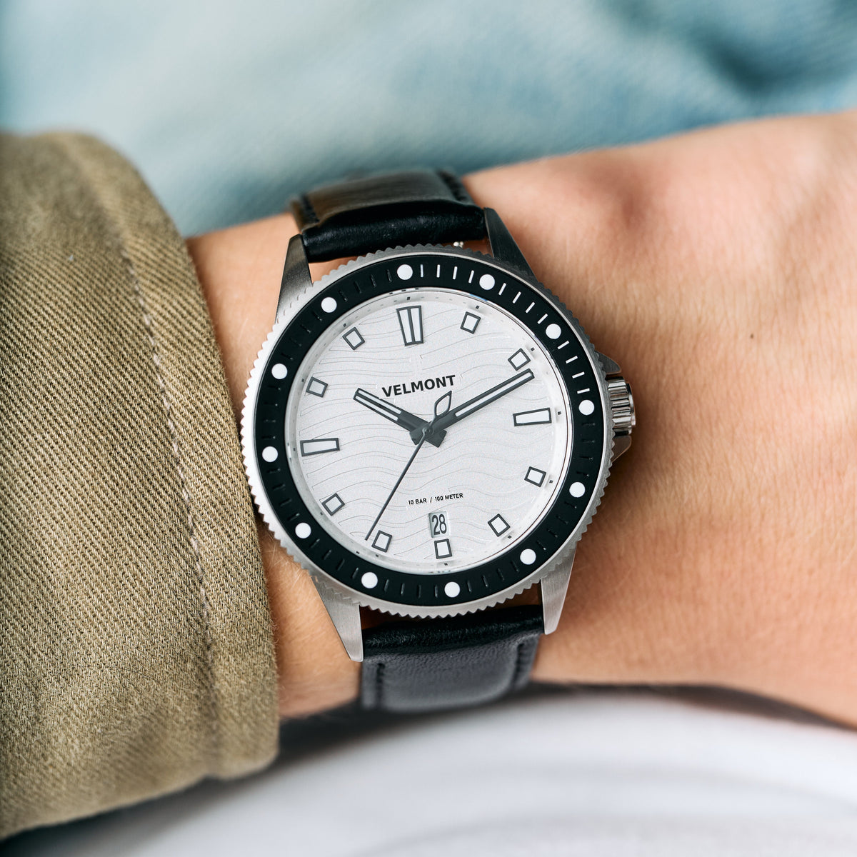White-dial watch with a black bezel worn beside an olive jacket cuff.