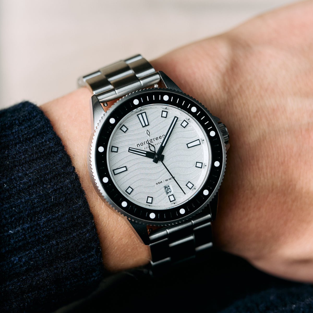 Silver-tone bracelet watch worn on a wrist next to a dark knit sleeve.