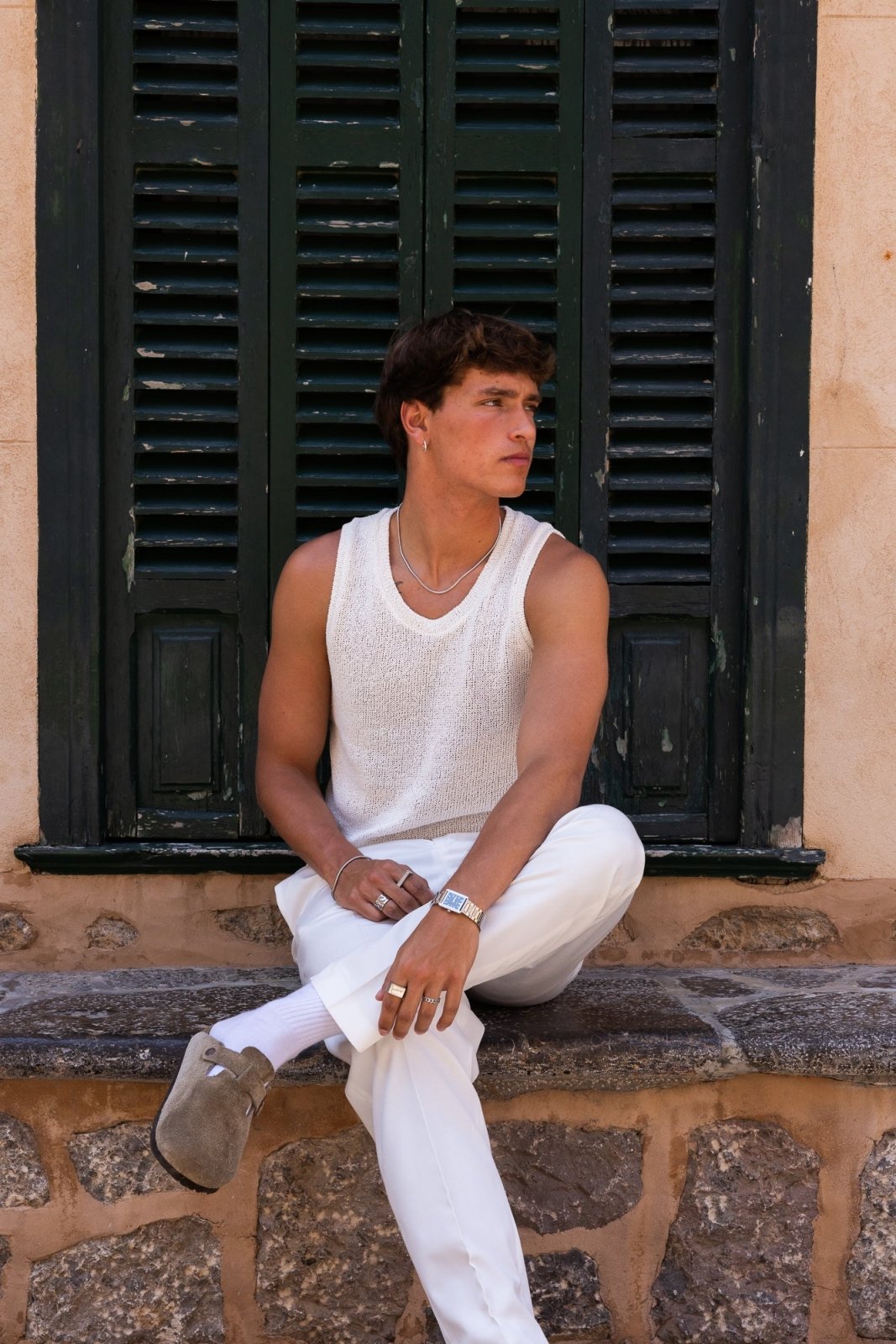 Man sitting by a shuttered window wearing the watch