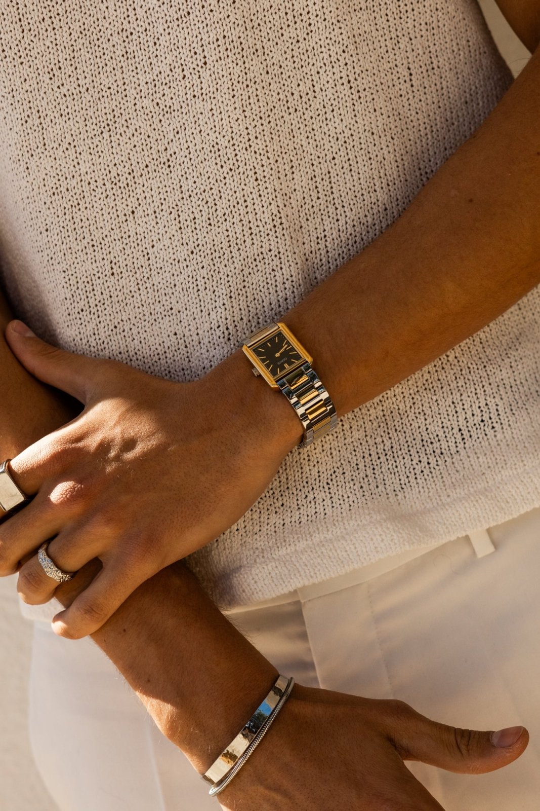 Arms crossed, gold-tone rectangular watch on the wrist