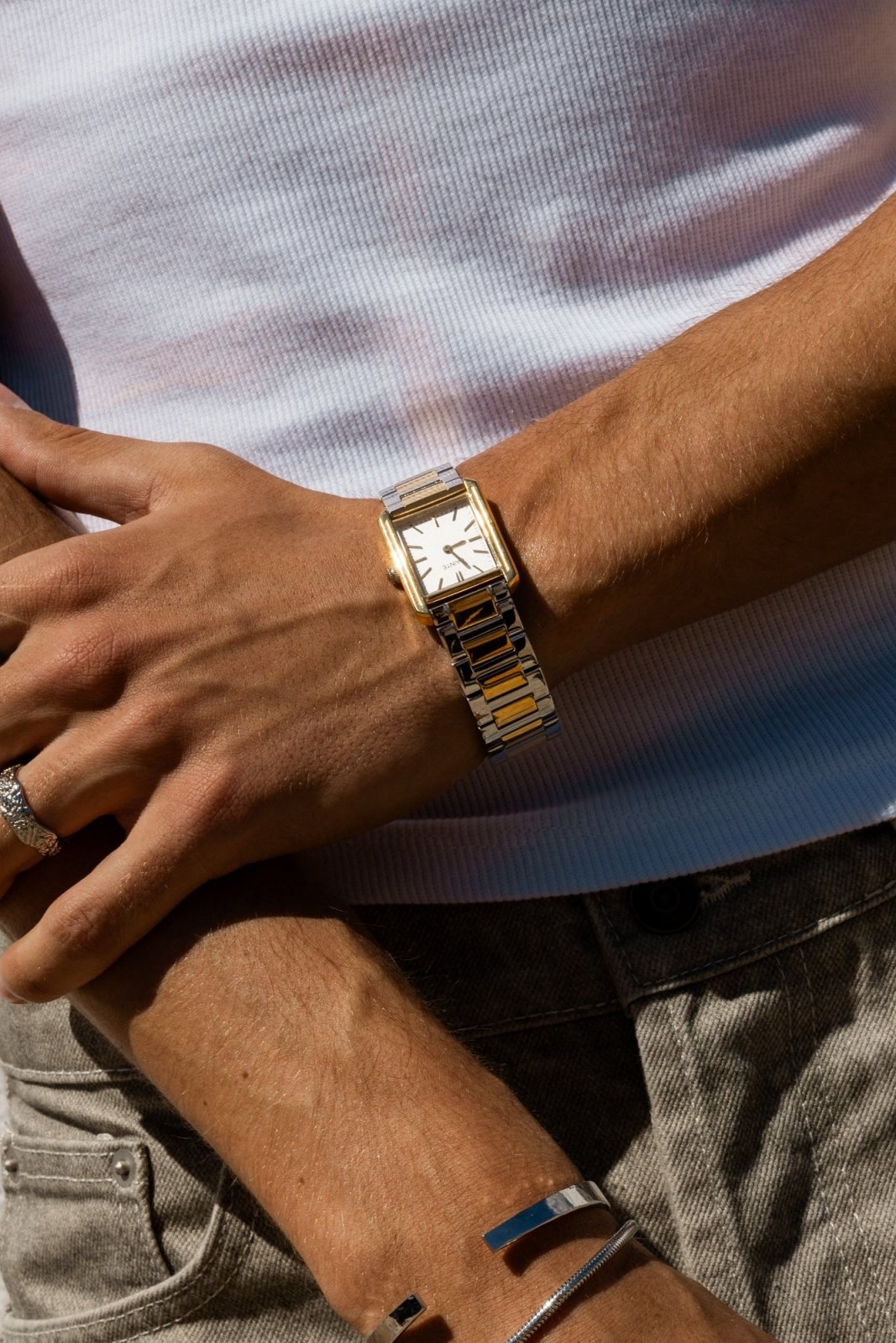Hands crossed over a white T-shirt, watch on the wrist