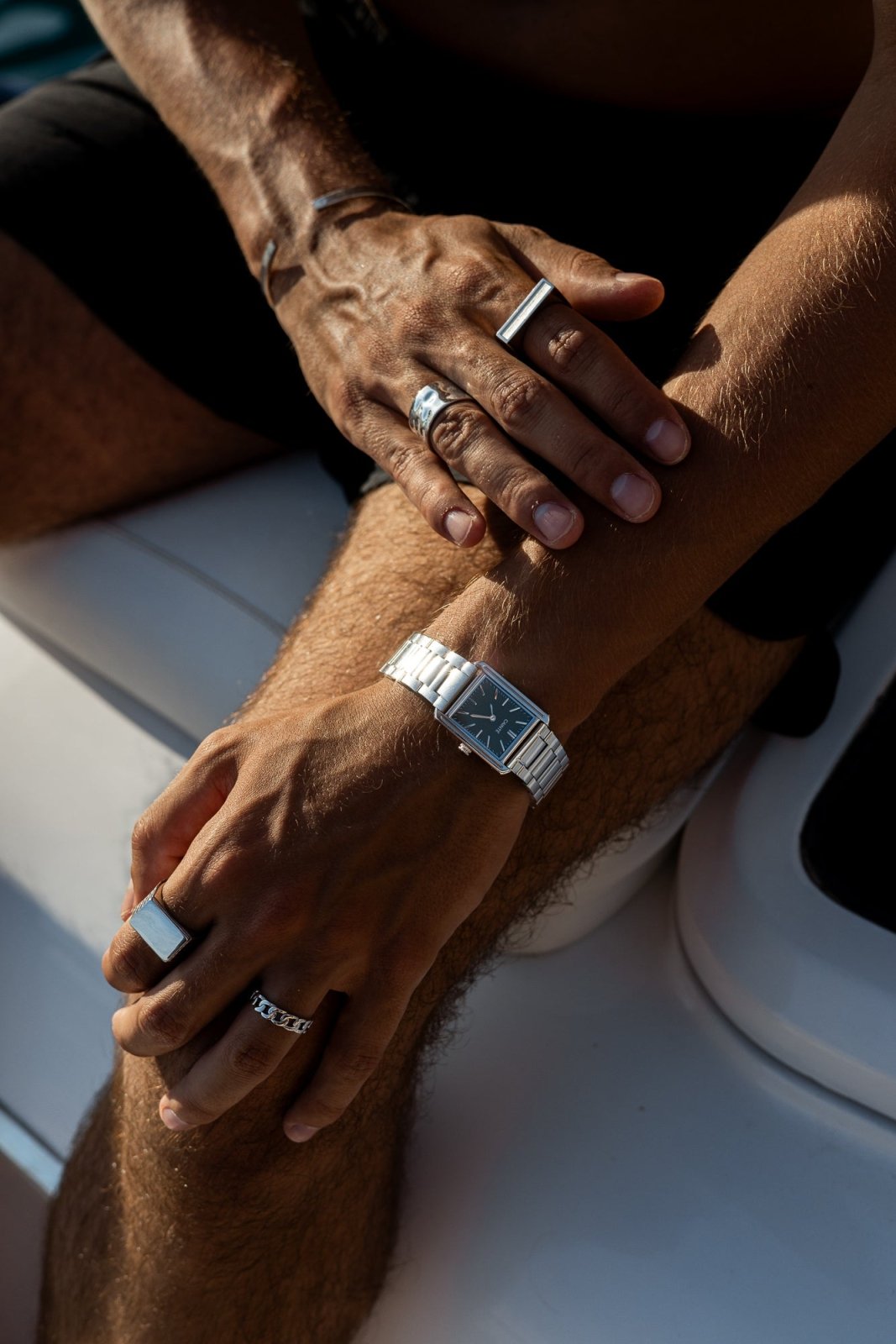 Hands resting on a boat, watch and rings visible