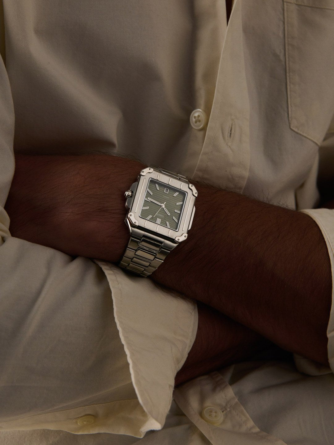 Arms crossed over a cream shirt, square watch on the wrist