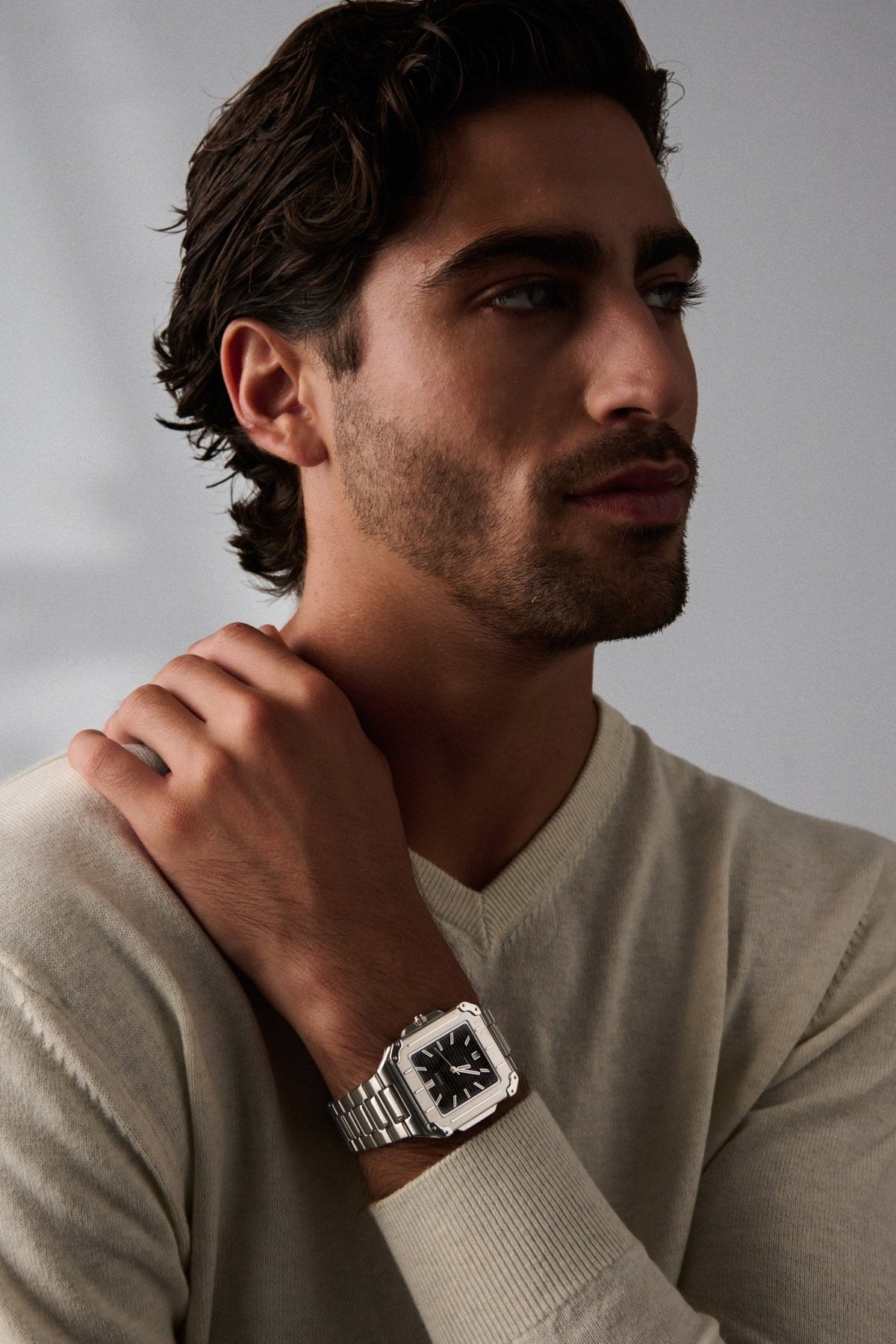 Man in a cream sweater, hand on shoulder, wearing the square watch