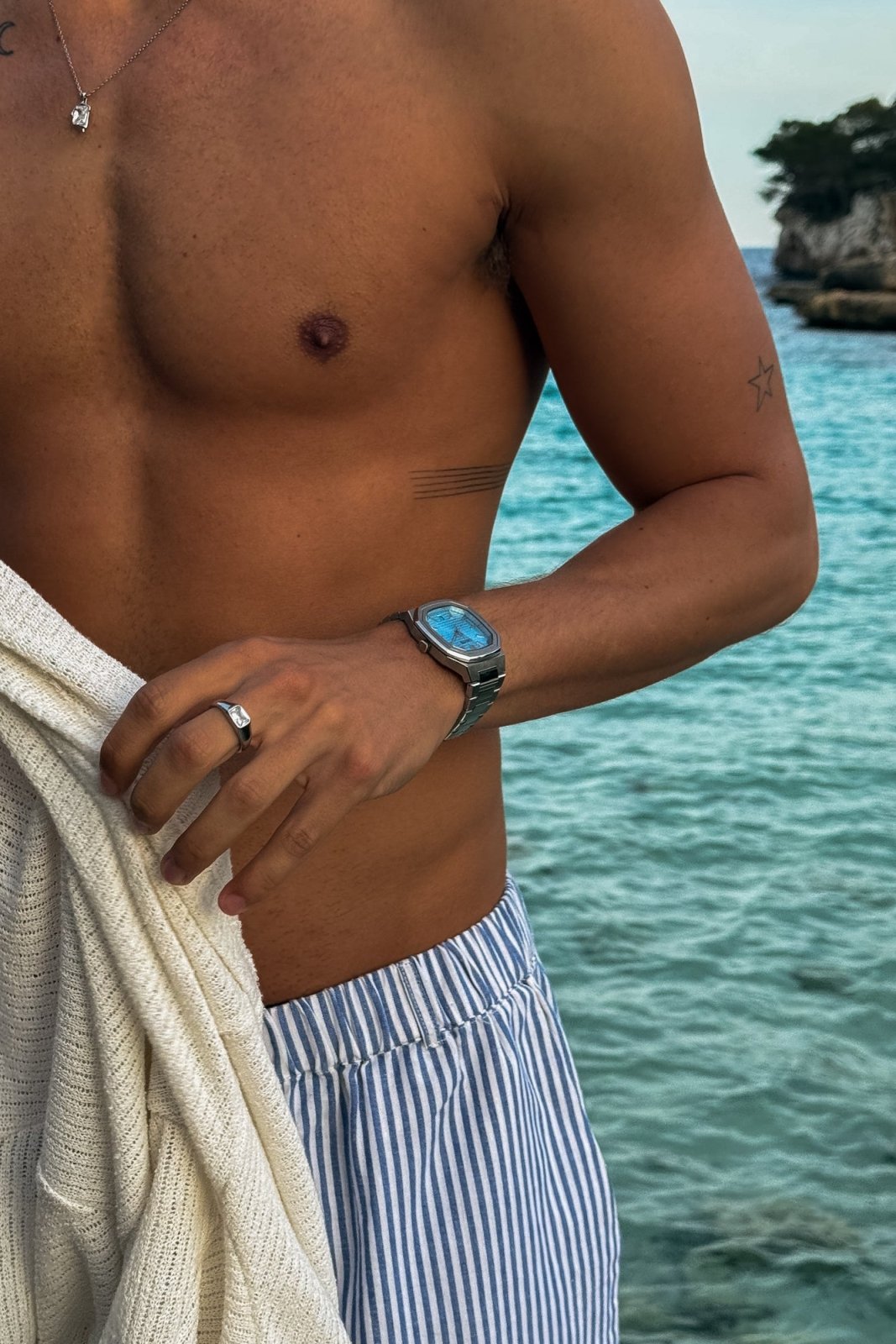 Man holding a knit towel by the sea, watch on the wrist
