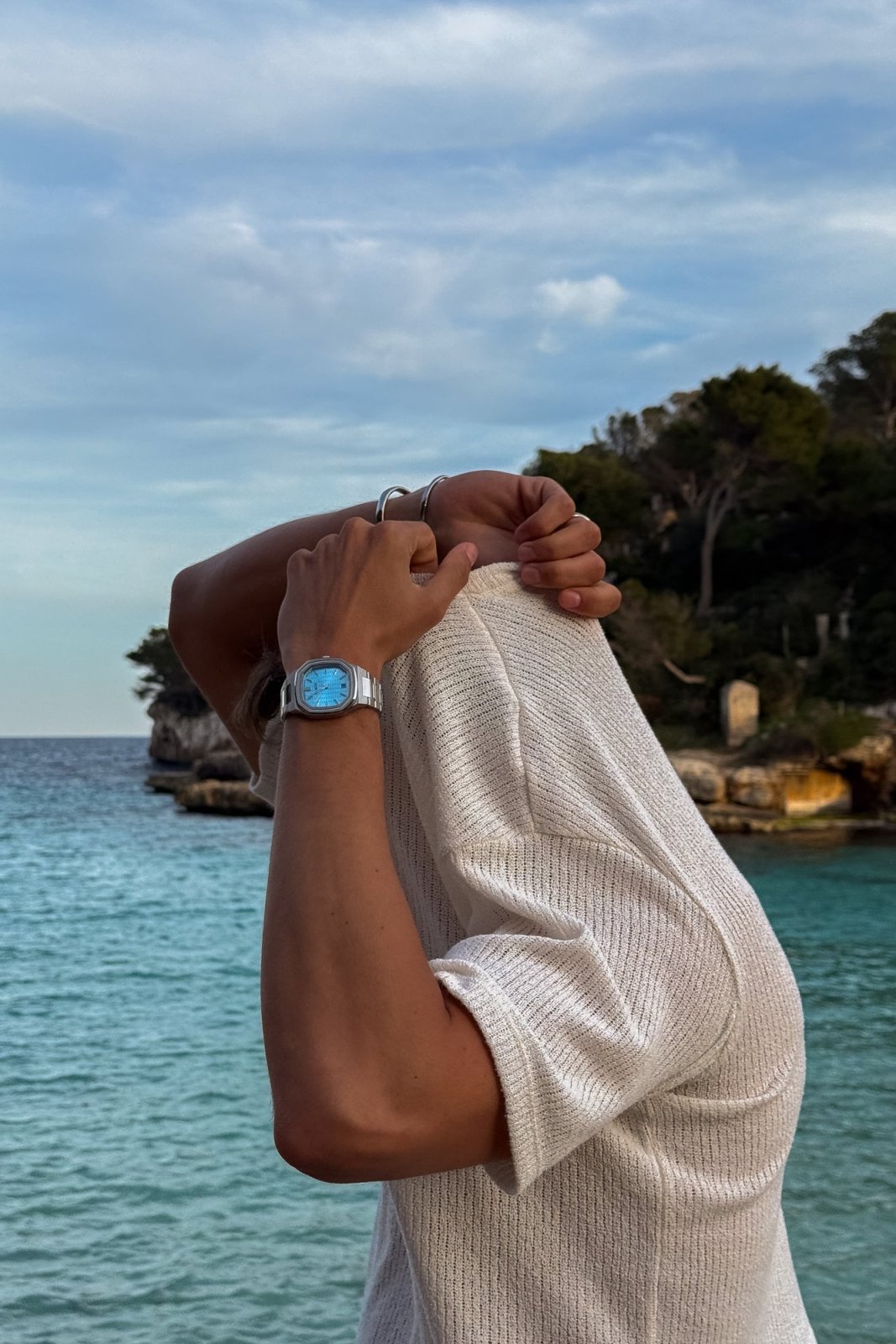 Man pulling on a knit shirt by the sea, watch visible