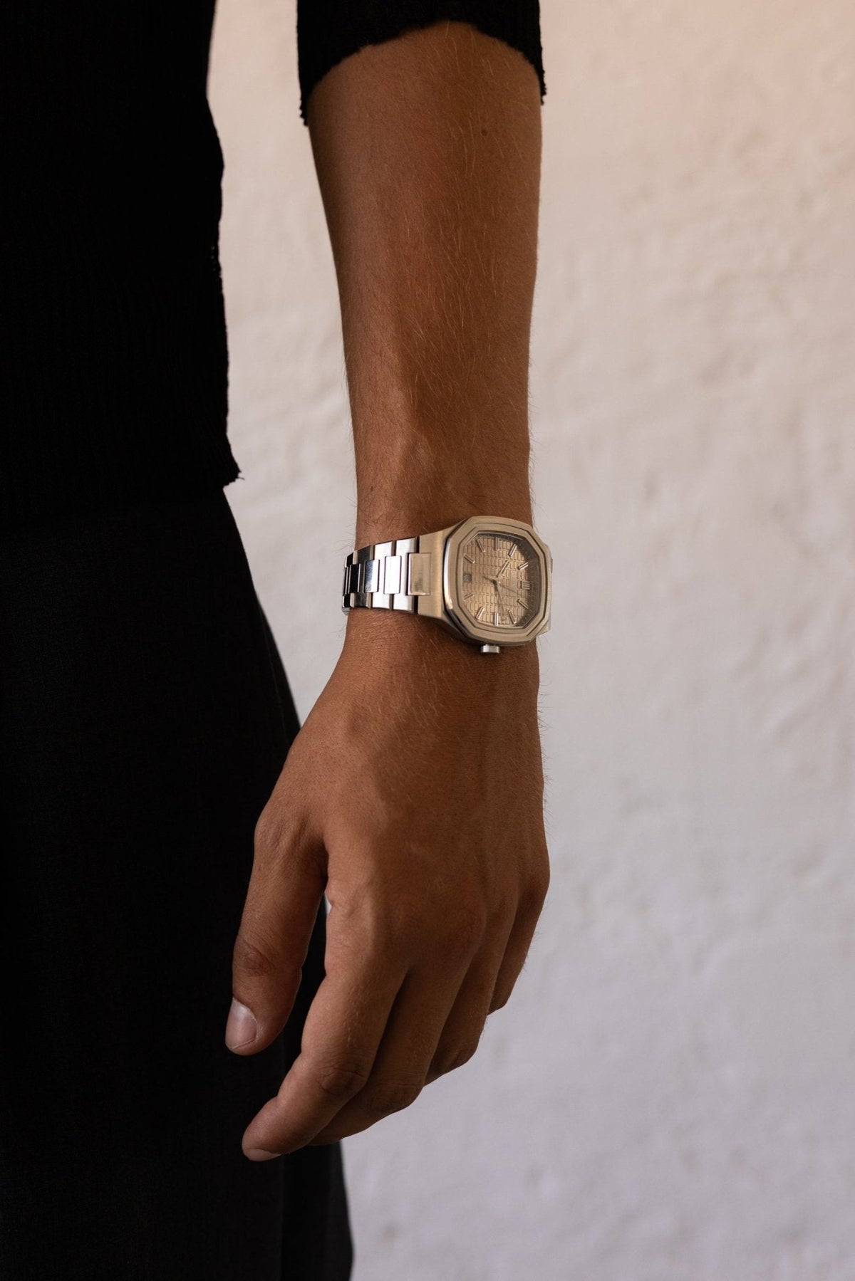Man in black standing by a white wall, watch on the wrist