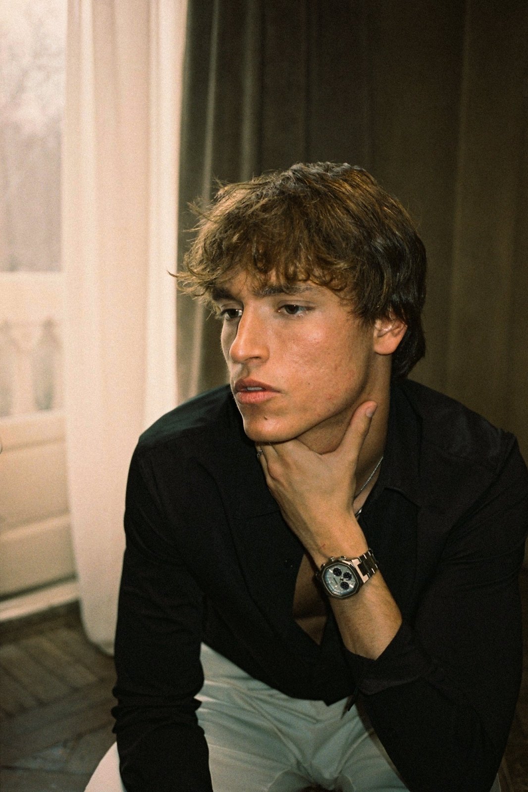 Man in a black shirt, hand at his chin, wearing the watch