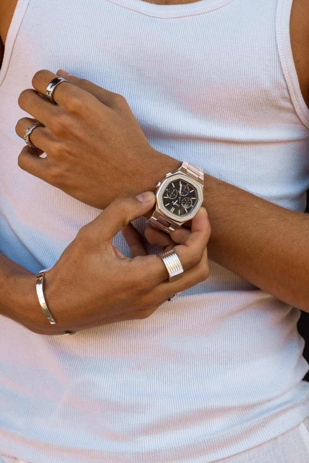 Hands adjusting the watch over a white tank top