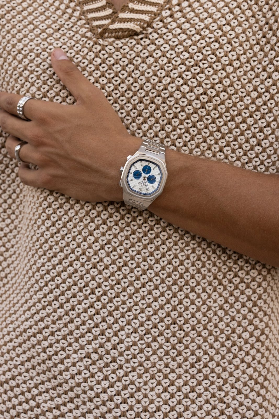 Wrist against a tan knit top, watch in view