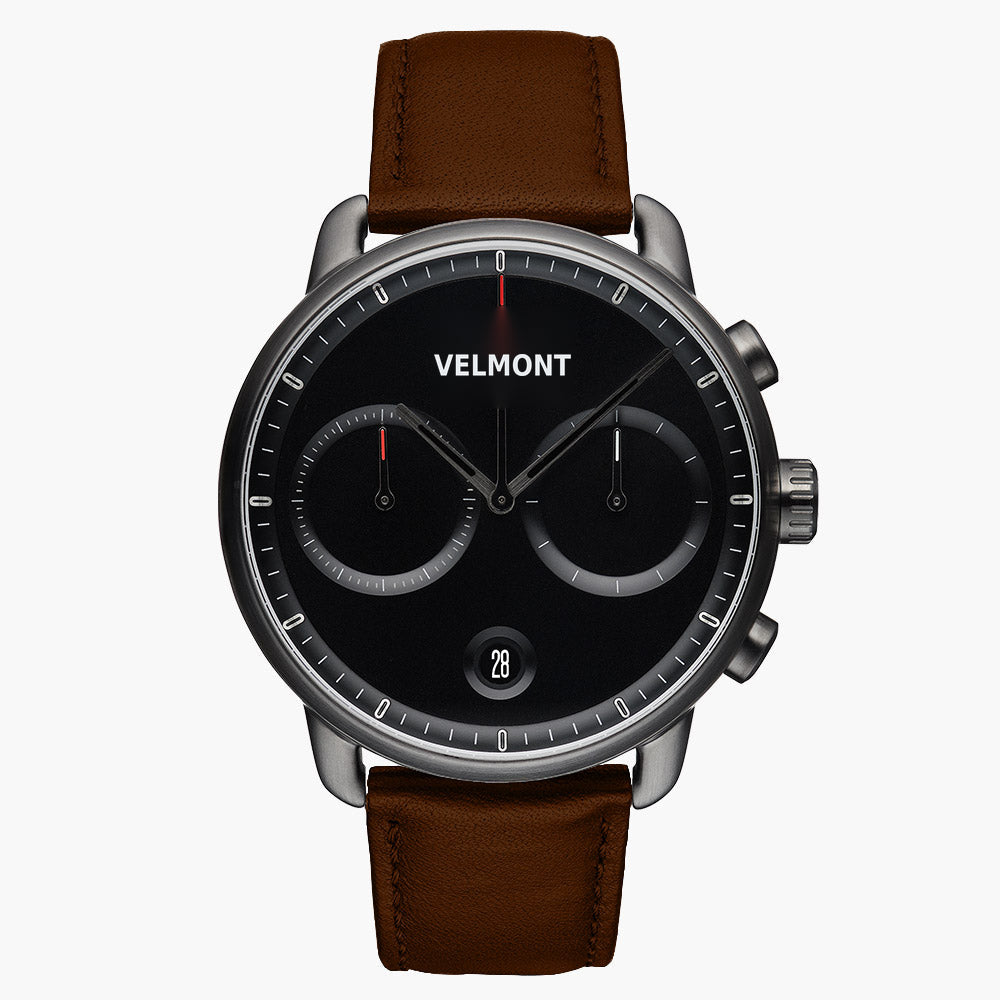 Chronograph-style watch with a black dial and gunmetal case on a brown strap.