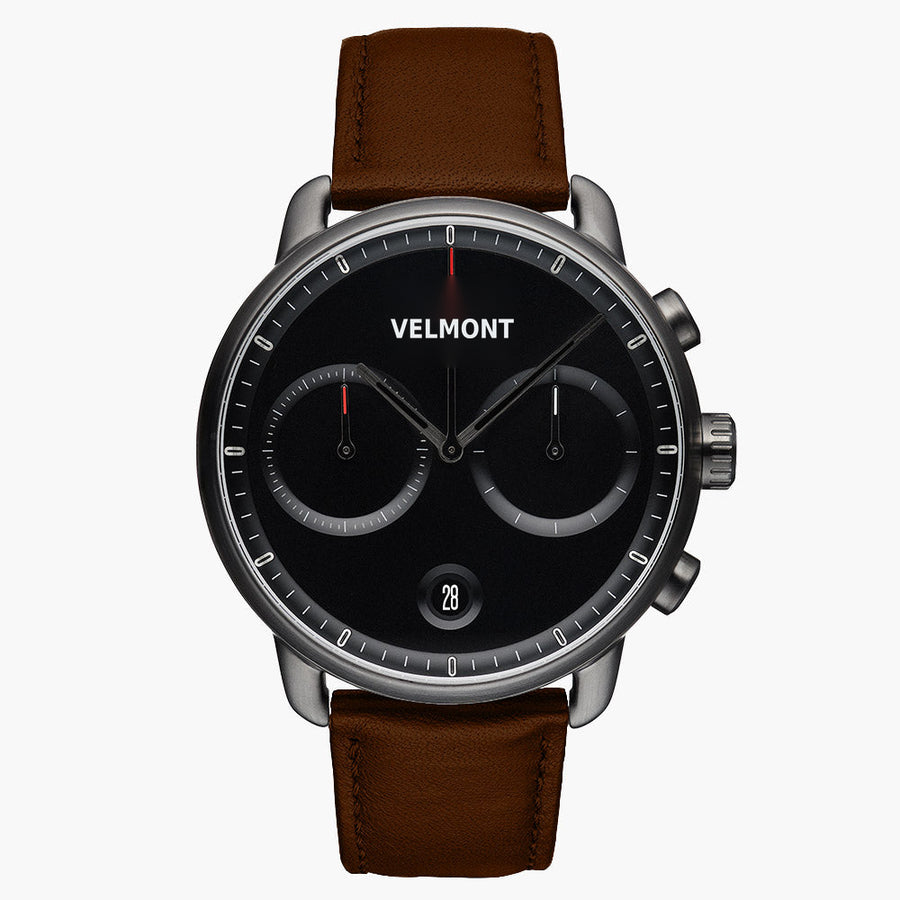 Chronograph-style watch with a black dial and gunmetal case on a brown strap.