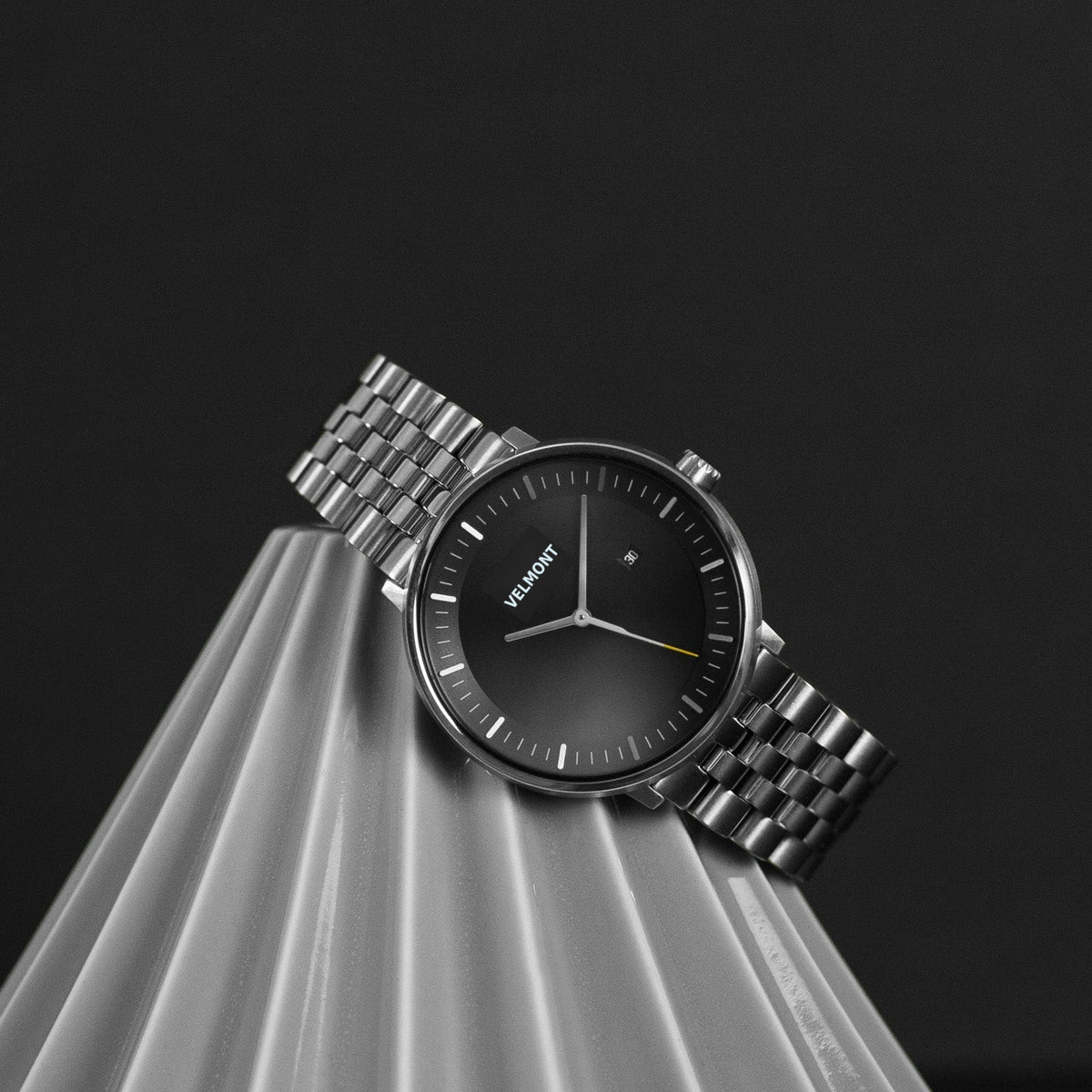 The watch resting on a pleated gray pedestal against a dark backdrop.