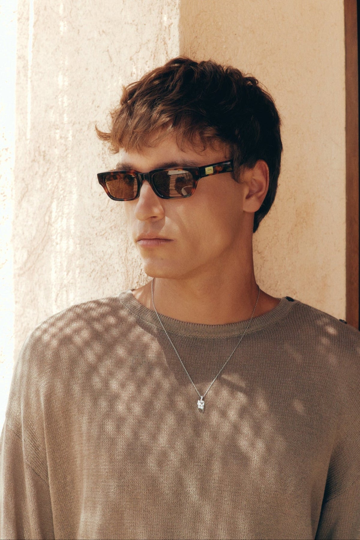 Man wearing the tortoise sunglasses against a sunny wall