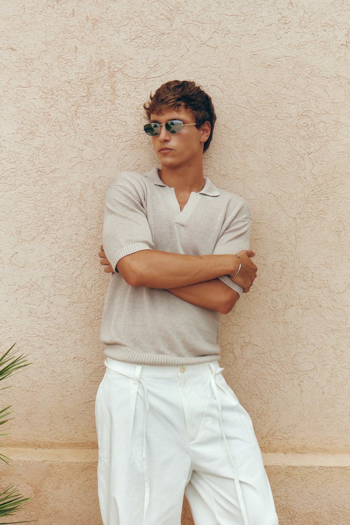 Man in a polo shirt wearing the sunglasses by a wall