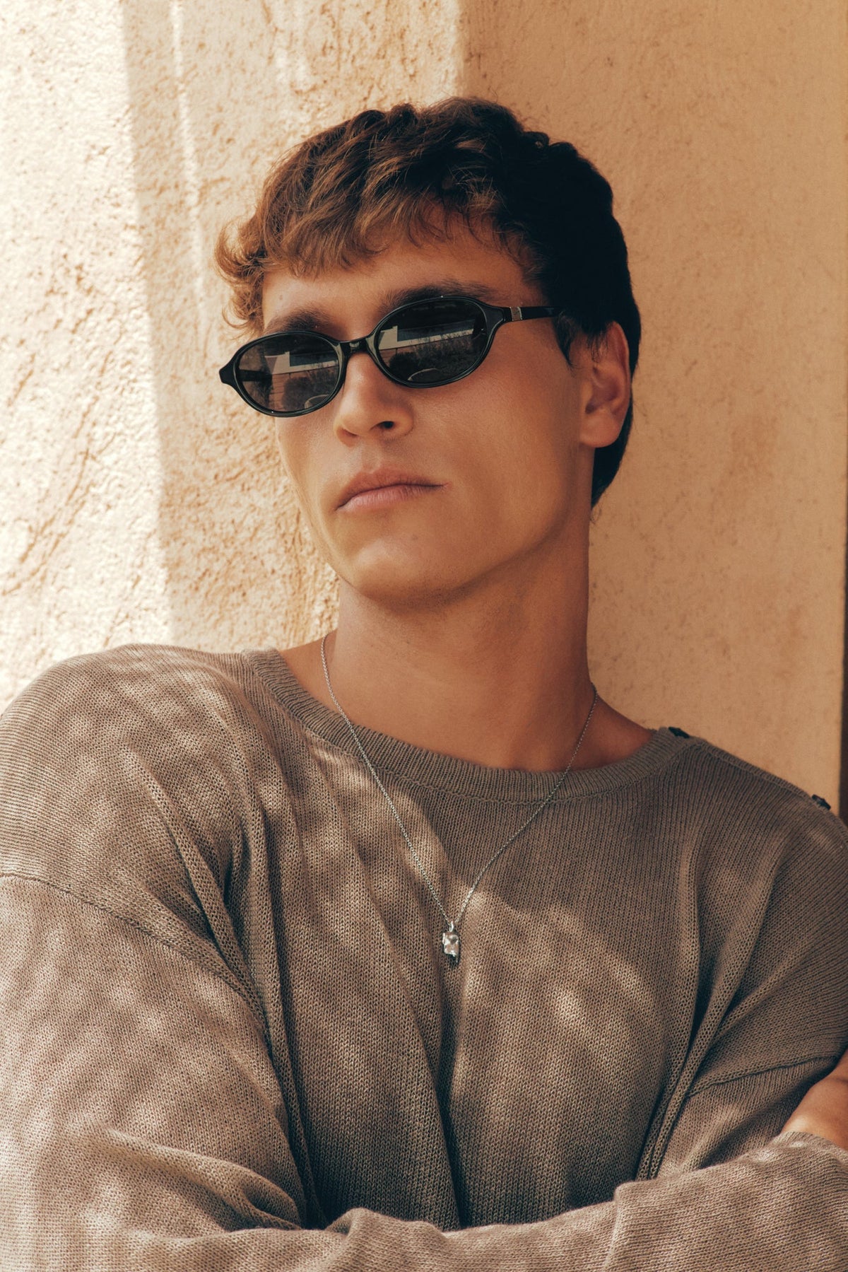 Man wearing the oval sunglasses against a wall