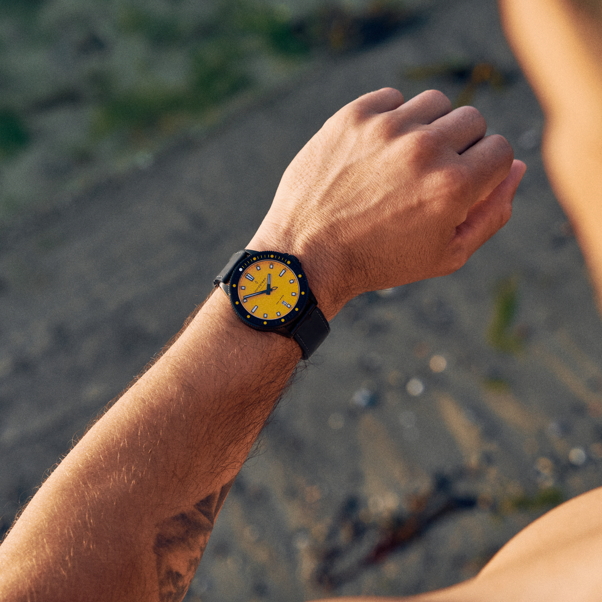Wrist shot of the black and yellow watch outdoors over sandy ground.