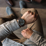 Gunmetal chronograph on the wrist of a seated man in gray