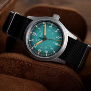 Teal blue dial field watch resting on a leather pouch