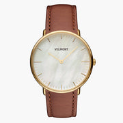 Small watch with a pearlescent white dial and gold-tone case on a brown strap.