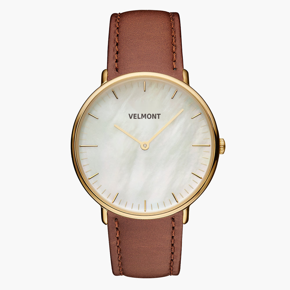 Small watch with a pearlescent white dial and gold-tone case on a brown strap.
