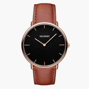 A black dial framed by a slim rose gold-tone case, set on a brown strap.