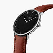 Three-quarter view of the watch showing the black dial and brown strap.